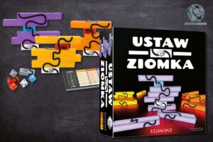 Pudełko z grą planszową Ustaw Ziomka obok rozłożonych elementów logicznej układanki na tle tablicy